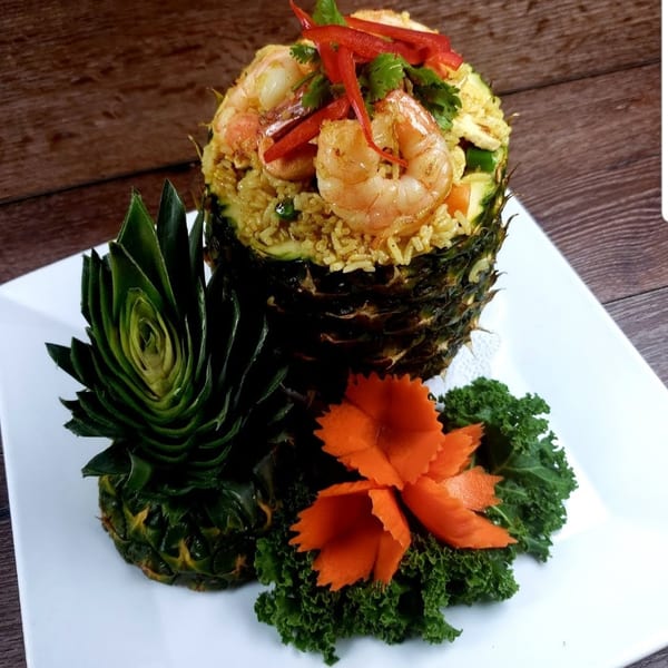 Pineapple fried rice with shrimp, red peppers, and cilantro, garnished with carved pineapple and carrots.