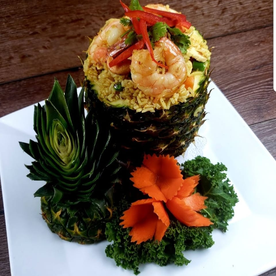 Pineapple fried rice with shrimp, red peppers, and cilantro, garnished with carved pineapple and carrots.