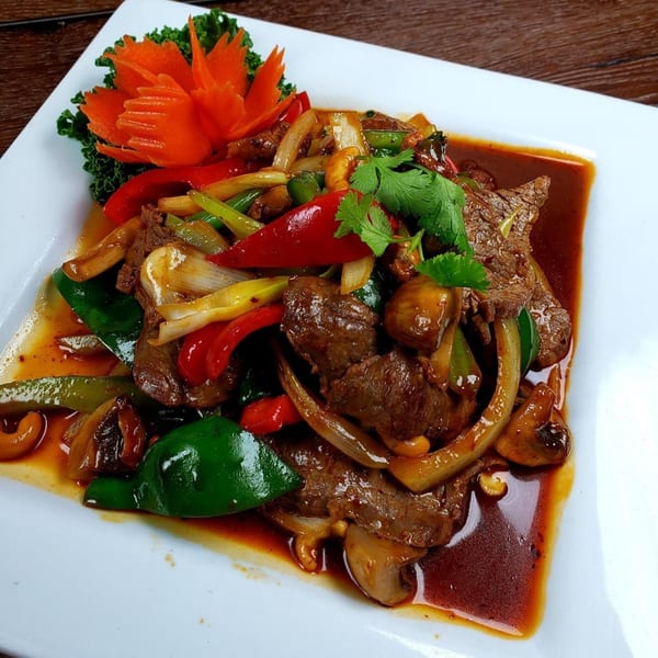 Thai beef stir-fry with red and green peppers, onions, mushrooms, and cashews, garnished with a carrot carving.