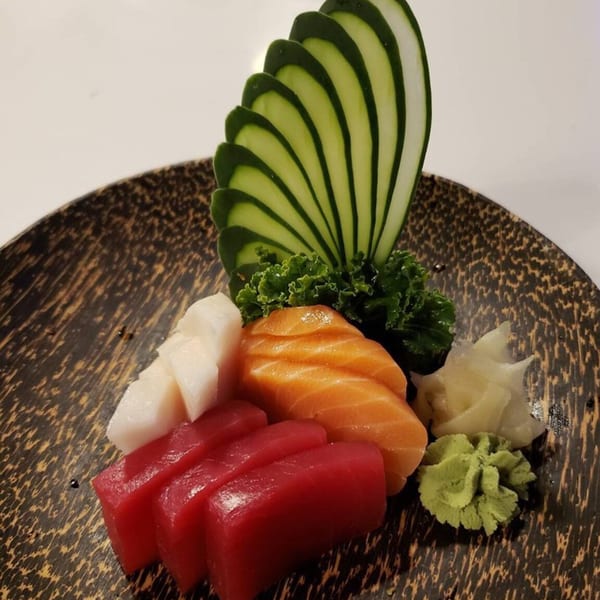Sashimi platter with tuna, salmon, and white fish, garnished with cucumber, lettuce, wasabi, and ginger.