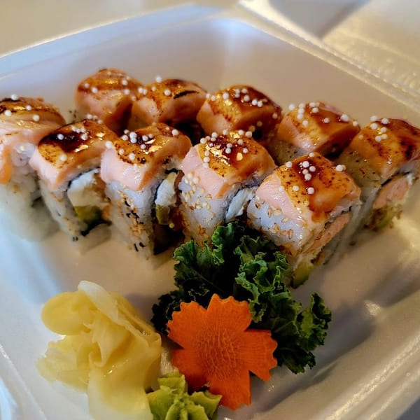 Sushi rolls with seared salmon, sauce, and white pearls, garnished with ginger, wasabi, and greens.