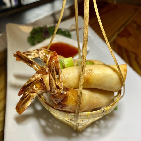 Crispy shrimp spring rolls in a bamboo basket, served with dipping sauce at Urban Thai & Sushi.
