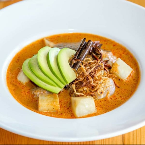 Close-up of a Thai dish with orange curry, avocado slices, fried onions, and white cubes.